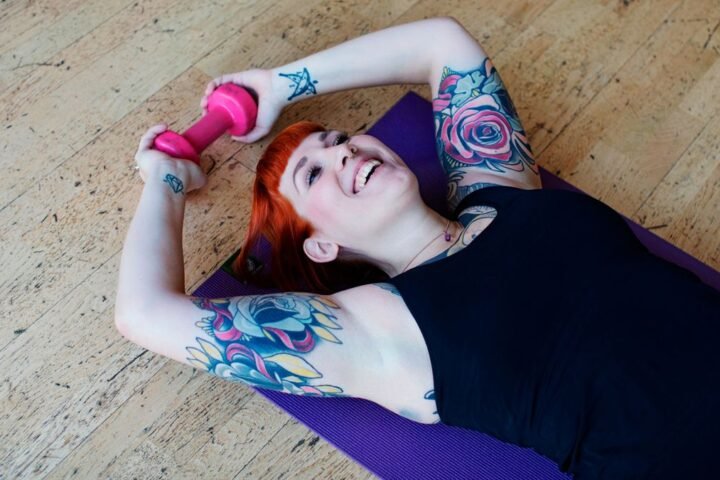 Woman lies on an exercise mat holding a dumbbell behind her head