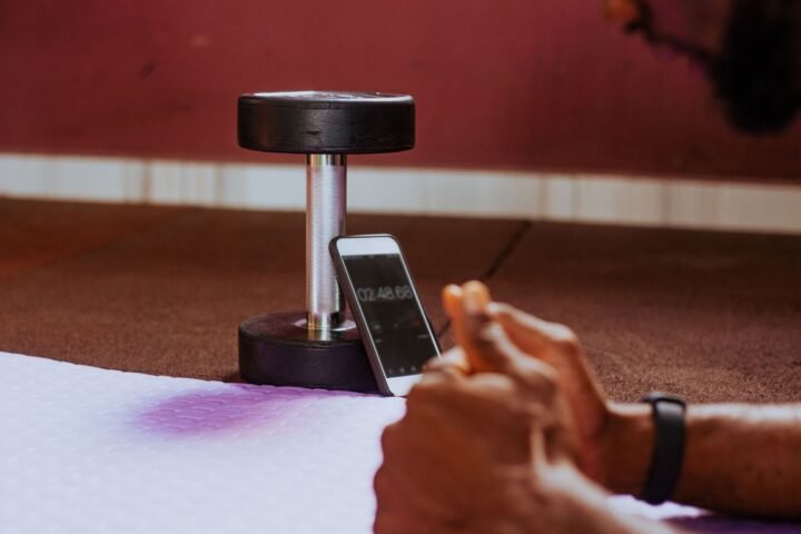 Man holding plank position looks at timer on smartphone, propped up on dumbbell