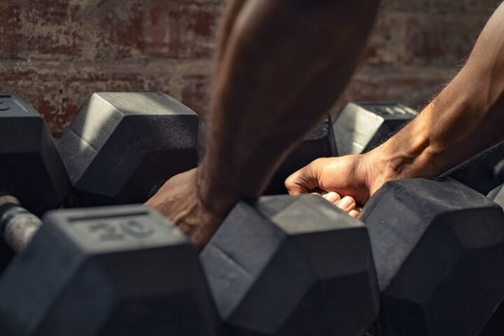 Hands picking up heavy dumbbells from rack