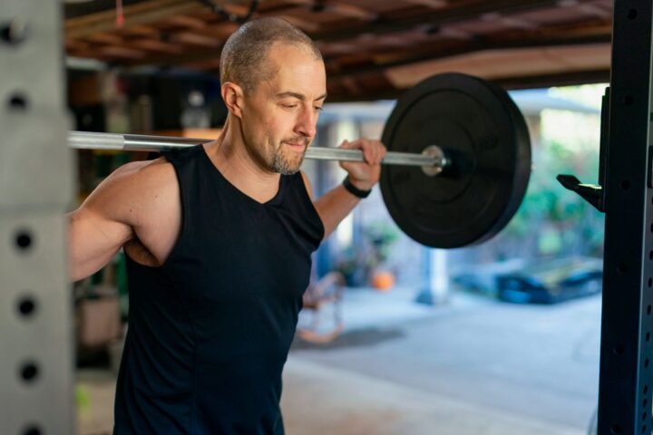 Man in his garage gym with a barbell over his shoulders next to a squat rack