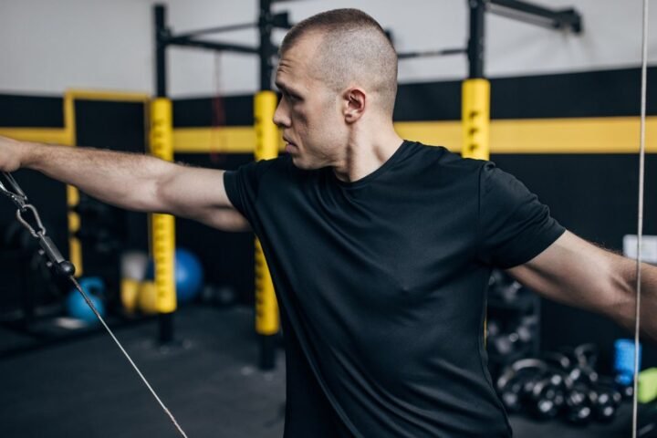 Man performs lateral raise using cable machine in gym