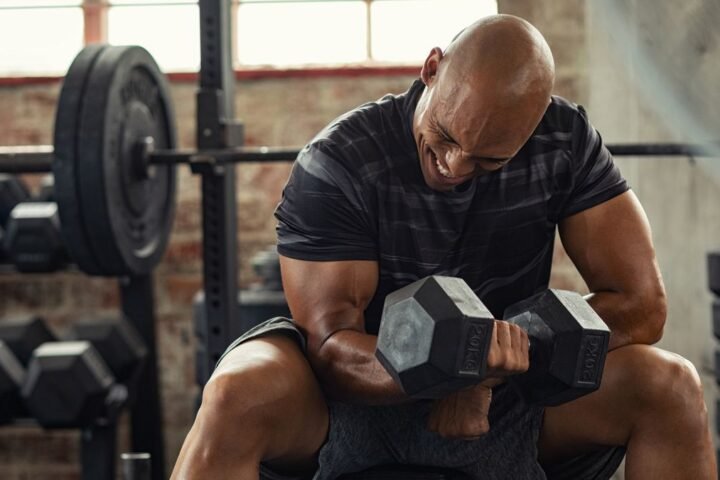 Man grimacing with effort as he performs a concentration curl in a gym